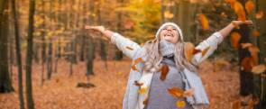 Frau wirft freudig Blätter in die Luft und steht im farbigen Herbst-Wald