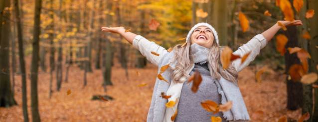 Frau wirft freudig Blätter in die Luft und steht im farbigen Herbst-Wald